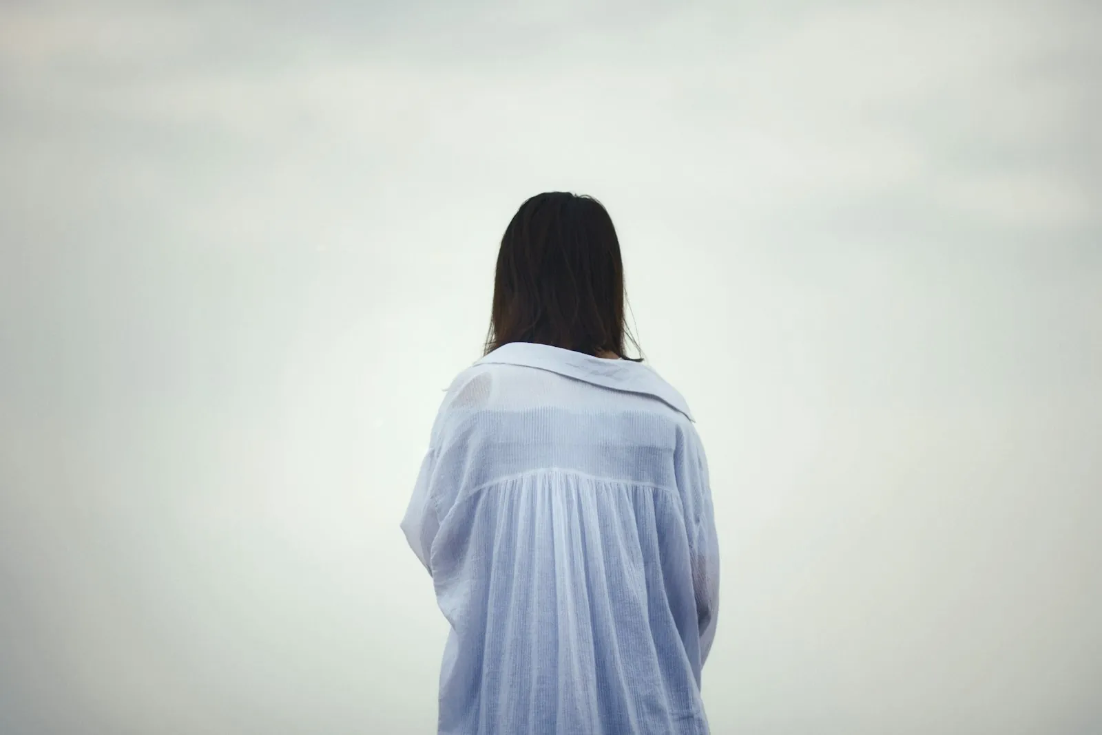 A person photographed from behind in soft daylight, wearing a loose white shirt. An illustrative photograph: not a patient of this practice, and not a depiction of results.