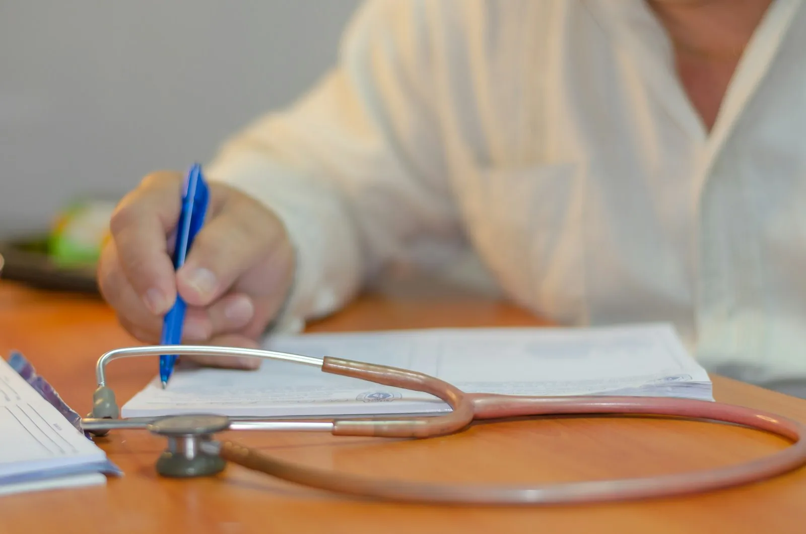 Hands writing notes at a desk beside a stethoscope. A representative photograph of a clinical consultation; it does not show Dr. Witoon or this practice.
