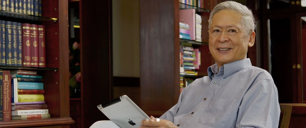 Dr. Witoon Wisuthseriwong seated in his study, in front of shelves of medical reference books.